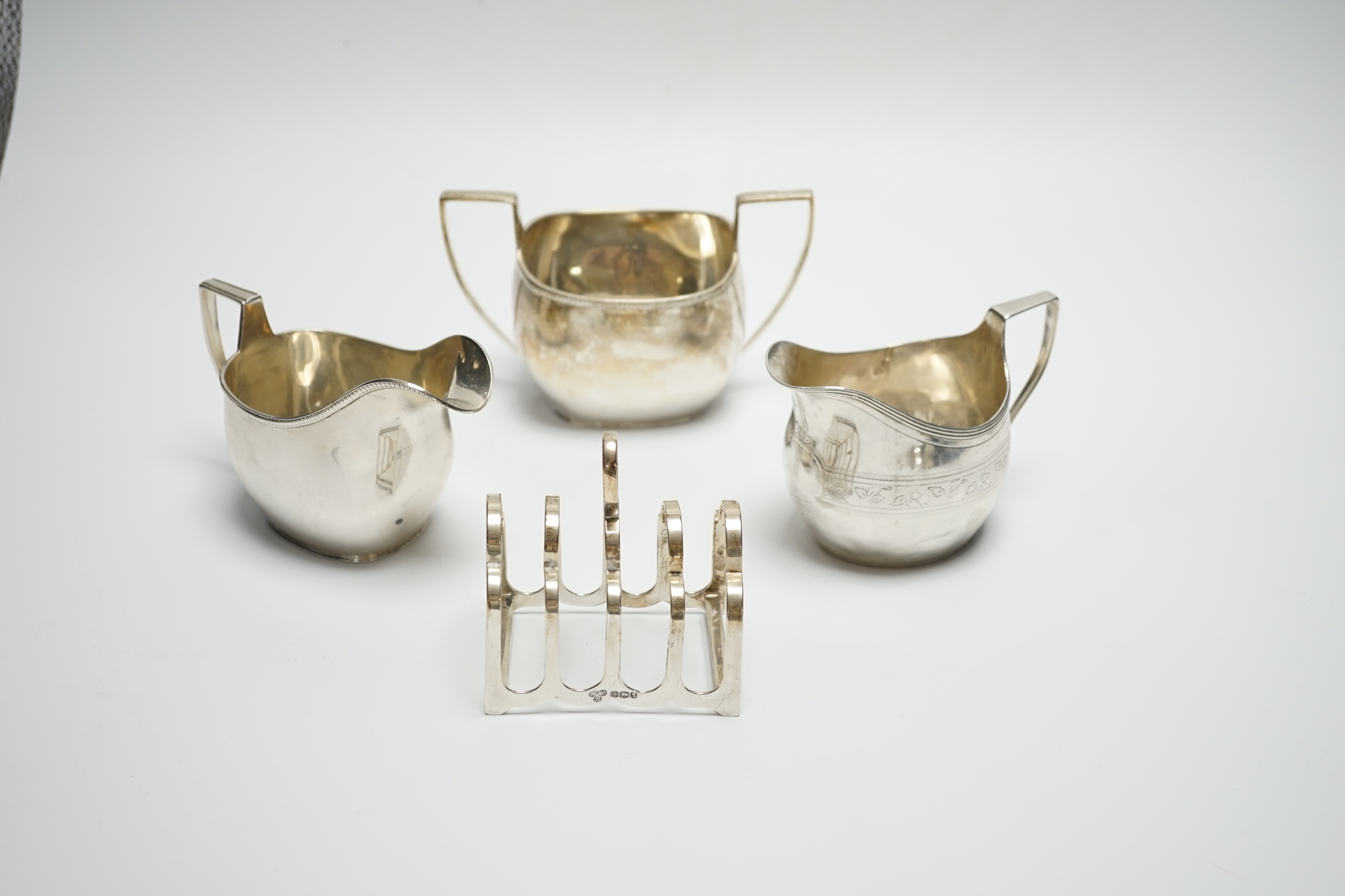 A George III engraved silver cream jug, London, 1808, height 82m, a George V silver cream jug and matching sugar bowl, and a George V silver five bar toast rack, 15.4oz.